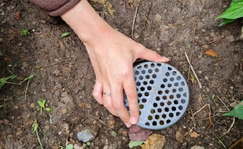 A hand holding a round metal grate

Description automatically generated